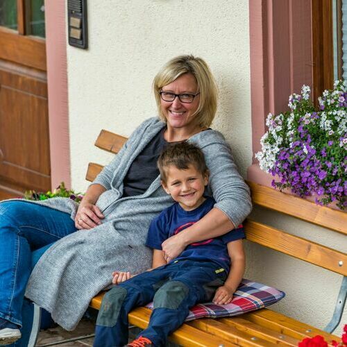 Eine Mutter und ihr Sohn sitzen auf einer Bank vor ihrer familienfreundlichen Unterkunft