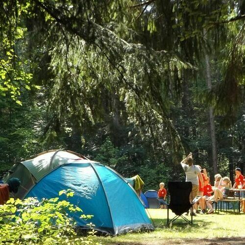 Zu sehen sind auf einer Zeltwiese zwei Zelte sowie G&auml;ste&comma; die auf einer Bank sitzen&period;