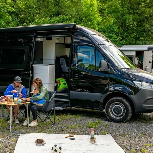 Ein Paar mit Kind sitzt vor seinem Camper&period; Im Hintergrund ist ein weiterer Camper zu sehen