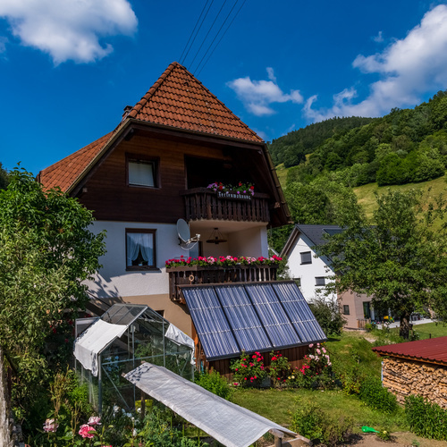 Au&szlig;enansicht des Haus Christel im Vordergrund ein Gartenbereich mit bl&uuml;henden Rosen und Gew&auml;chshaus - 