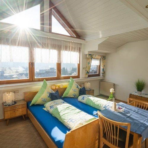 Doppelbett mit gro&szlig;er Fensterfront im Hintergrund und kleinem Tisch - 