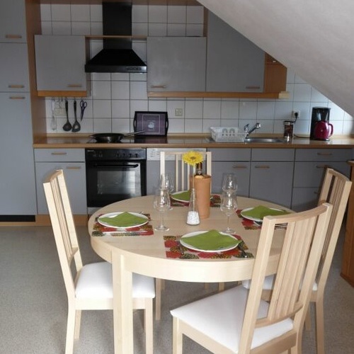 runder Esstisch mit vier St&uuml;hlen im Hintergrund die K&uuml;chenzeile - 