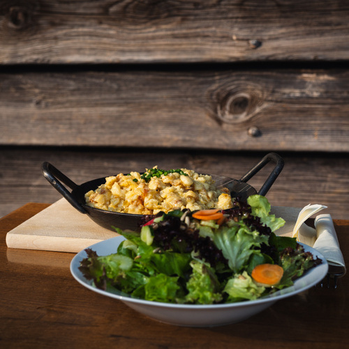 Salatteller und eine Servierpfanne mit K&auml;sekn&ouml;pfle im Hintergrund  - 